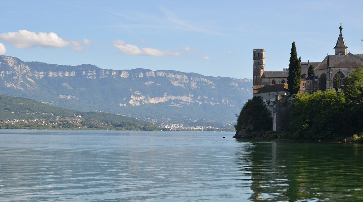 castle-like building sits on bank of still blue water with mountains in the distance